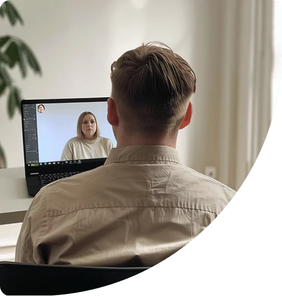 En person sitter ved et skrivebord og deltar i en videosamtale på laptopen sin med en kvinne som vises på skjermen. Rommet er lyst og minimalistisk innredet.